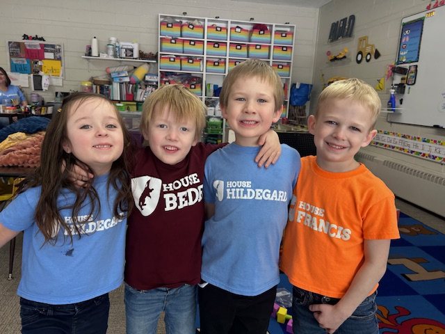 Four lower school students in their house t-shirts smiling in a classroom