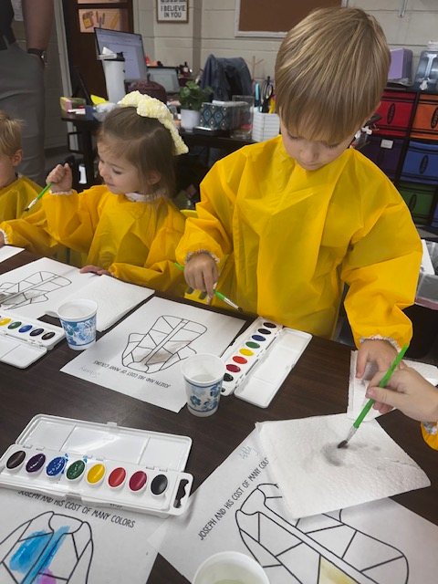 A kindergarten student in a yellow smock painting with watercolors